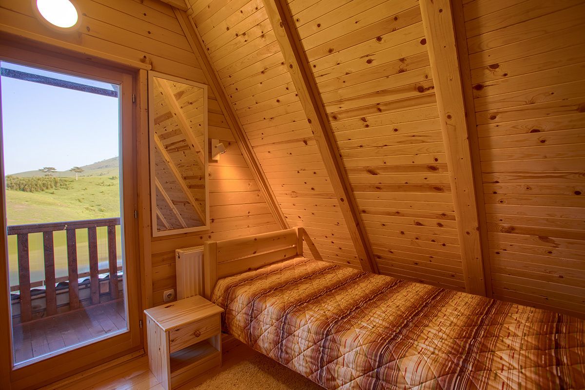 A small, cozy room with a sloped ceiling, a single bed, a small table, and a window with a view of a grassy field.