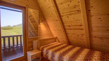 A small, cozy room with a sloped ceiling, a single bed, a small table, and a window with a view of a grassy field.