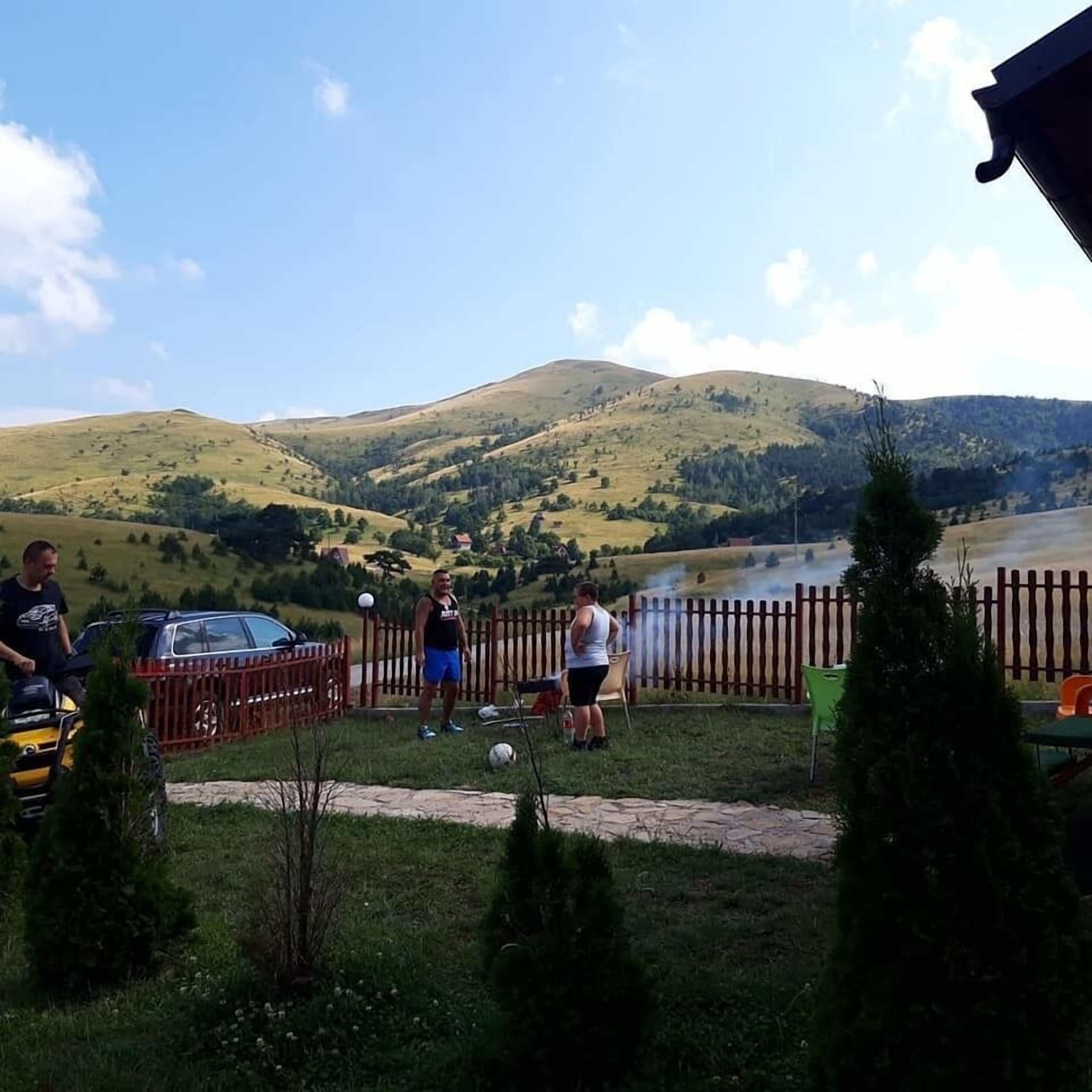 A rural outdoor setting with a wooden fence, a parked car, and a person on a quad bike.