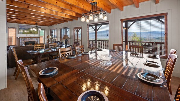 Ruime eethoek met een grote houten tafel, meerdere stoelen en uitzicht op de bergen door grote ramen.