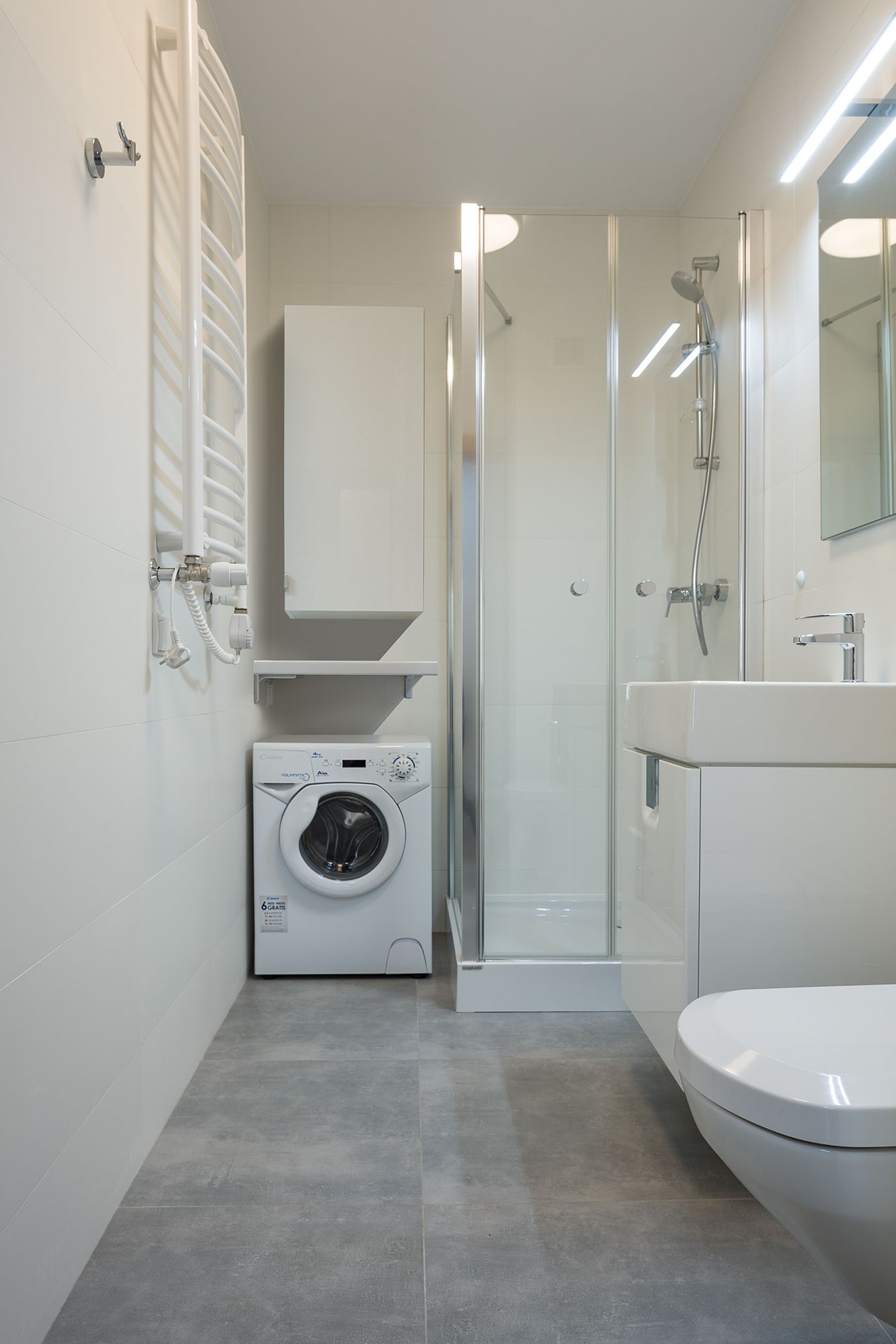 A modern bathroom with a glass-enclosed shower, a built-in washing machine, and a toilet.