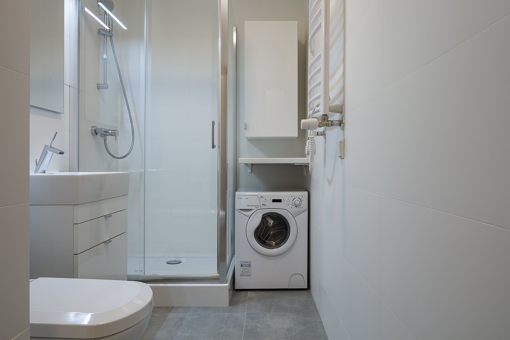 Une salle de bain compacte comprenant des toilettes, un lavabo, une douche et un lave-linge à chargement frontal.
