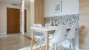 A modern dining area with a white table and chairs, a wooden door, and a wall with a pebble pattern. - Apartamenty Sun&Snow Wczasowa Południowe (Ustka)