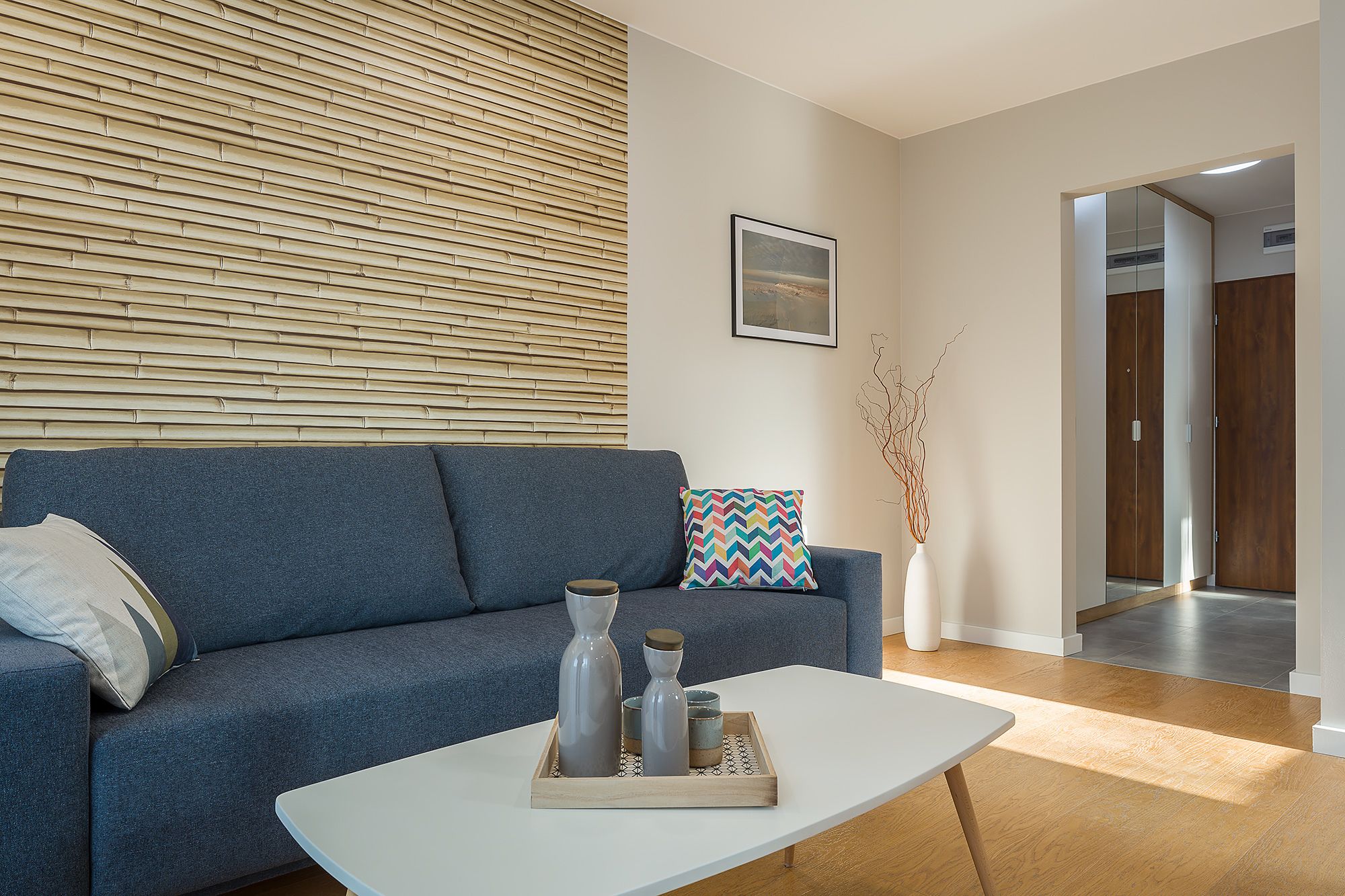 A modern living room with a sofa, a coffee table with decorative items, a wall-mounted picture, and a wooden wall panel.