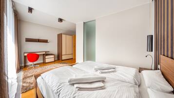 A modern hotel room with a large bed, a desk, a red chair, and a wardrobe.