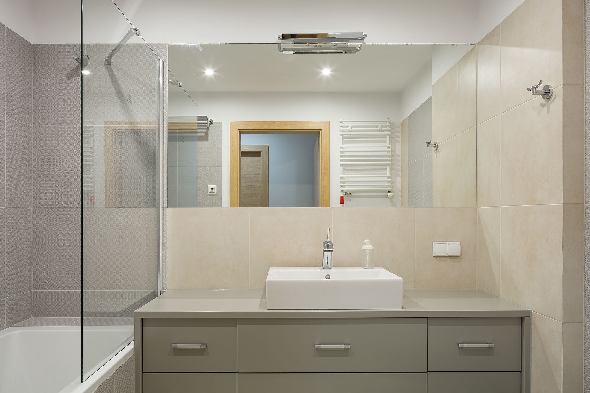 A modern bathroom with a glass shower enclosure, a white sink, and a vanity with drawers.