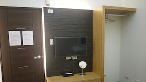 A modern room with a dark wood wardrobe, a flat-screen TV mounted on a wooden panel, a small wooden console table with a mirror, and a wooden shelf with a hanging item. - Fishmoon Homestay (Magong)