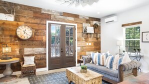 Un salon avec un mur en bois, une horloge, un canapé agrémenté de coussins à rayures, une table basse et un fauteuil en osier.