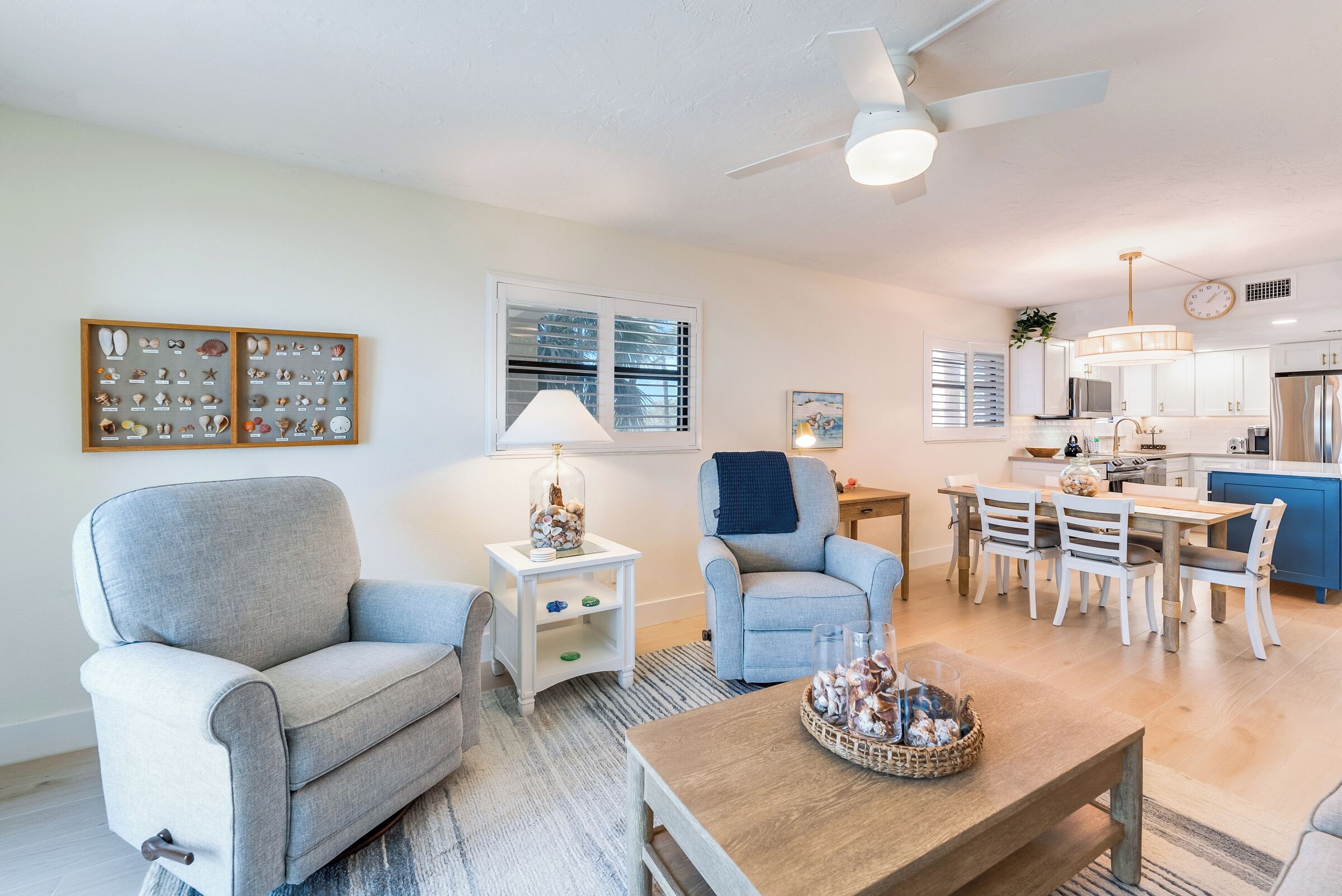 A modern living room with grey sofas, a wooden coffee table, and a dining area with white chairs.