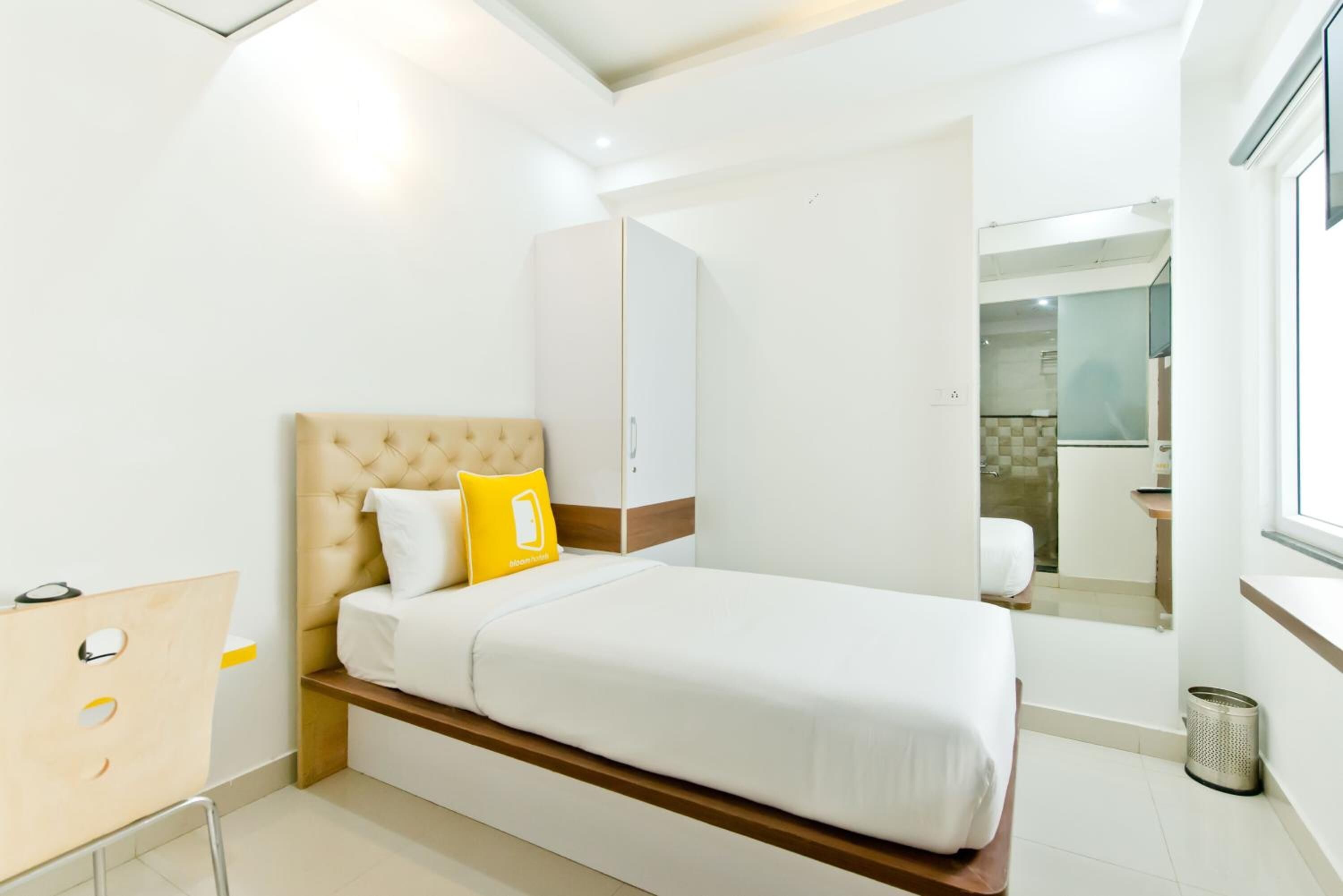 A modern hotel room with a bed, a wardrobe, a small desk, and a bathroom visible through an open door.