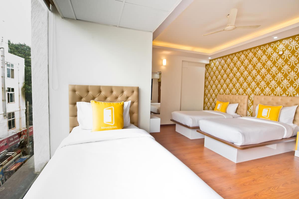 Une chambre d’hôtel avec un grand lit, deux petits lits, un ventilateur de plafond et un mur décoré de motifs.