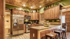 Una cocina con armarios de madera, un refrigerador de acero inoxidable, una encimera de granito y un taburete de bar.