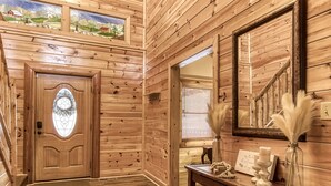 Un interior de madera con una puerta, un espejo, una mesa con adornos y una ventana con persianas.