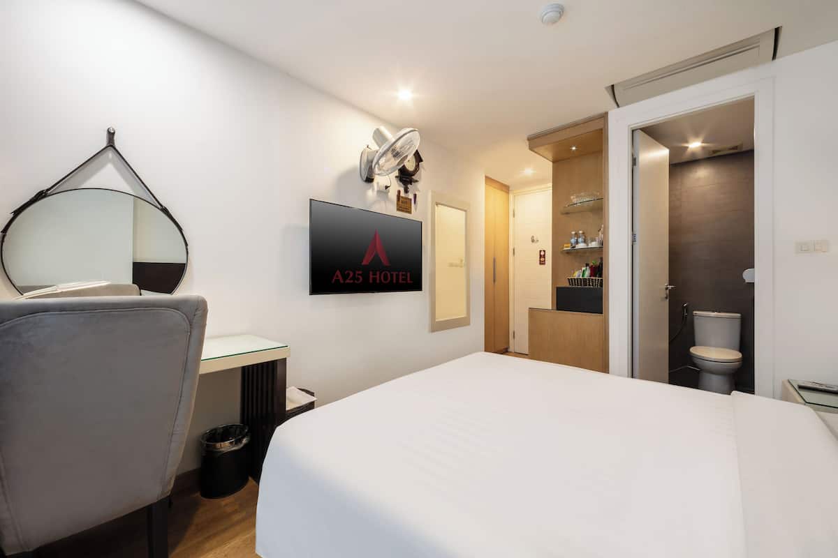 A hotel room with a bed, a desk, a chair, a TV mounted on the wall, and a bathroom visible through an open door.