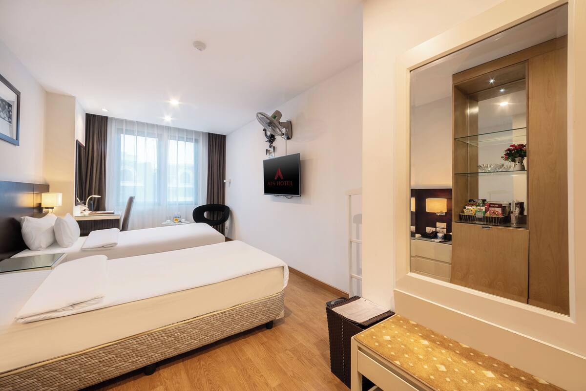 A hotel room with two beds, a desk, a chair, a TV, and a large mirror.