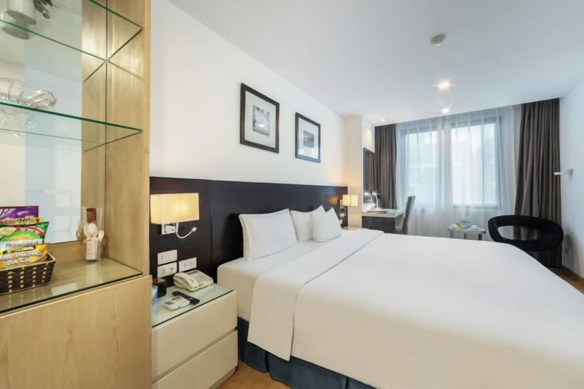 A hotel room with a large bed, bedside tables, a desk, and a chair.