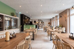 A spacious restaurant with wooden tables and chairs, a green accent wall, and a variety of dishes displayed on shelves. - Emma's B&B LUNGERN - Self Check-in Hotel (Lungern)