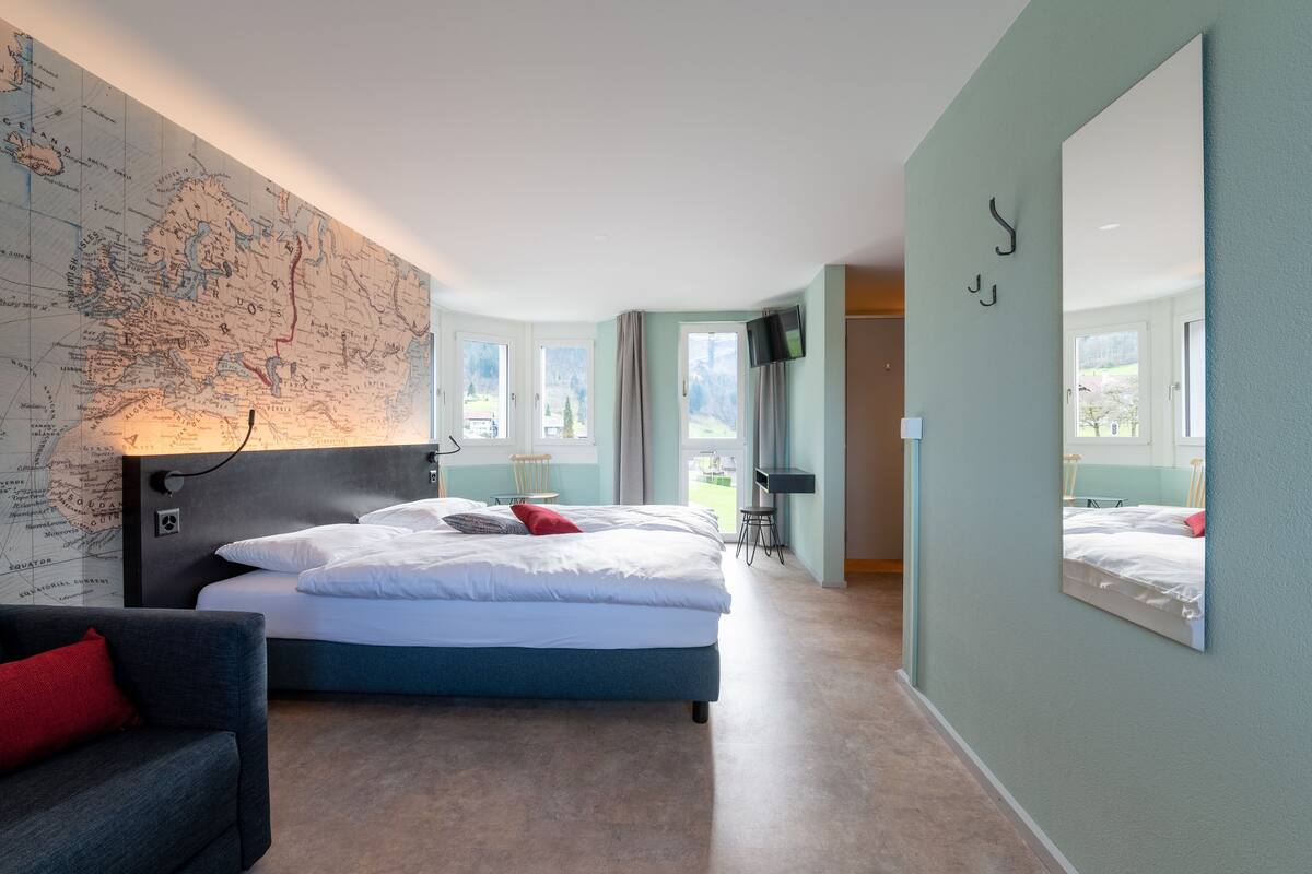 Habitación de hotel moderna con una cama grande, un mapa en la pared, un televisor y vistas al exterior.