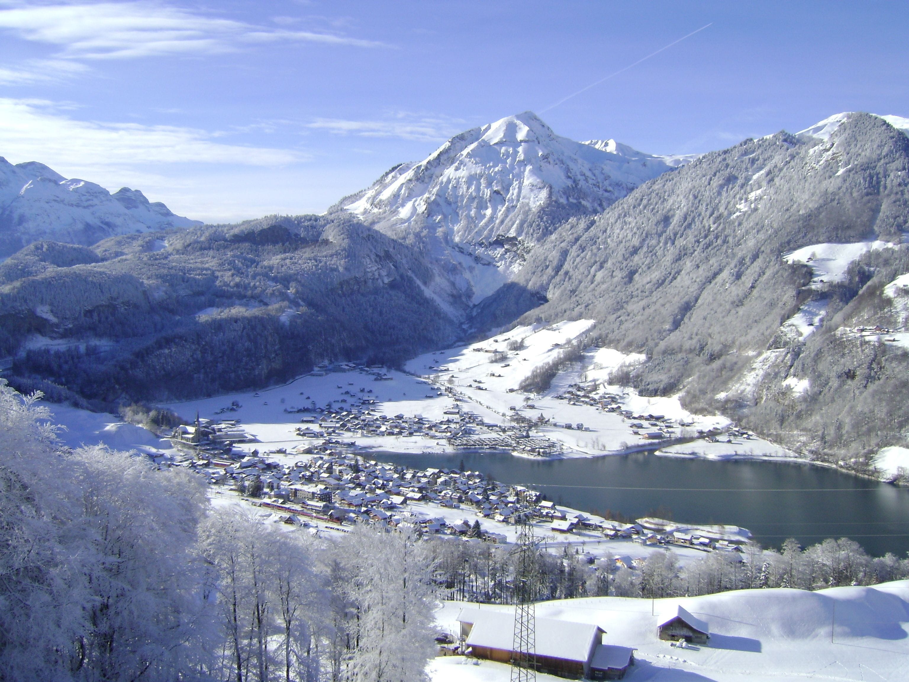 A snow-covered mountain landscape with a town nestled at the base, surrounded by snow-covered trees and a lake.