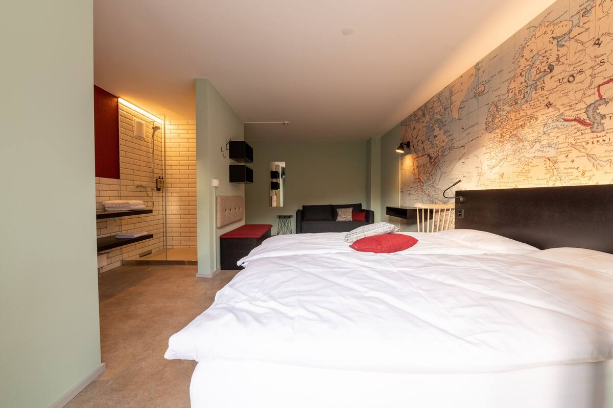 Un dormitorio con una cama grande, un mapa en la pared, una zona de ducha y un pequeño rincón de descanso.