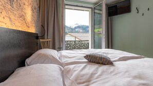 Una habitación de hotel con una cama grande, un mapa en la pared, una ventana con vistas a montañas y un televisor montado en la pared.