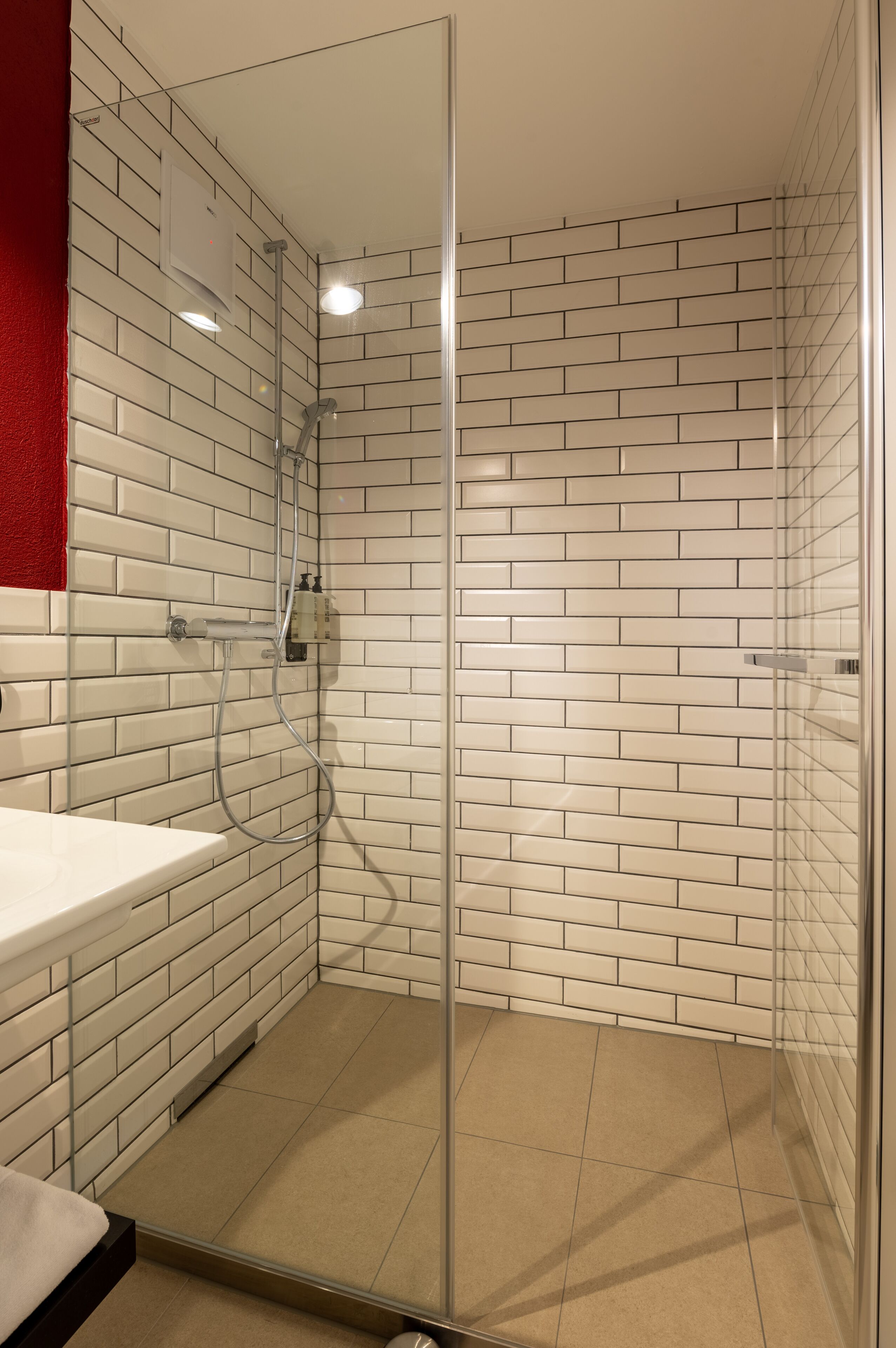 Un baño moderno con cabina de ducha de vidrio, azulejos blancos tipo metro y una pared de acento roja.