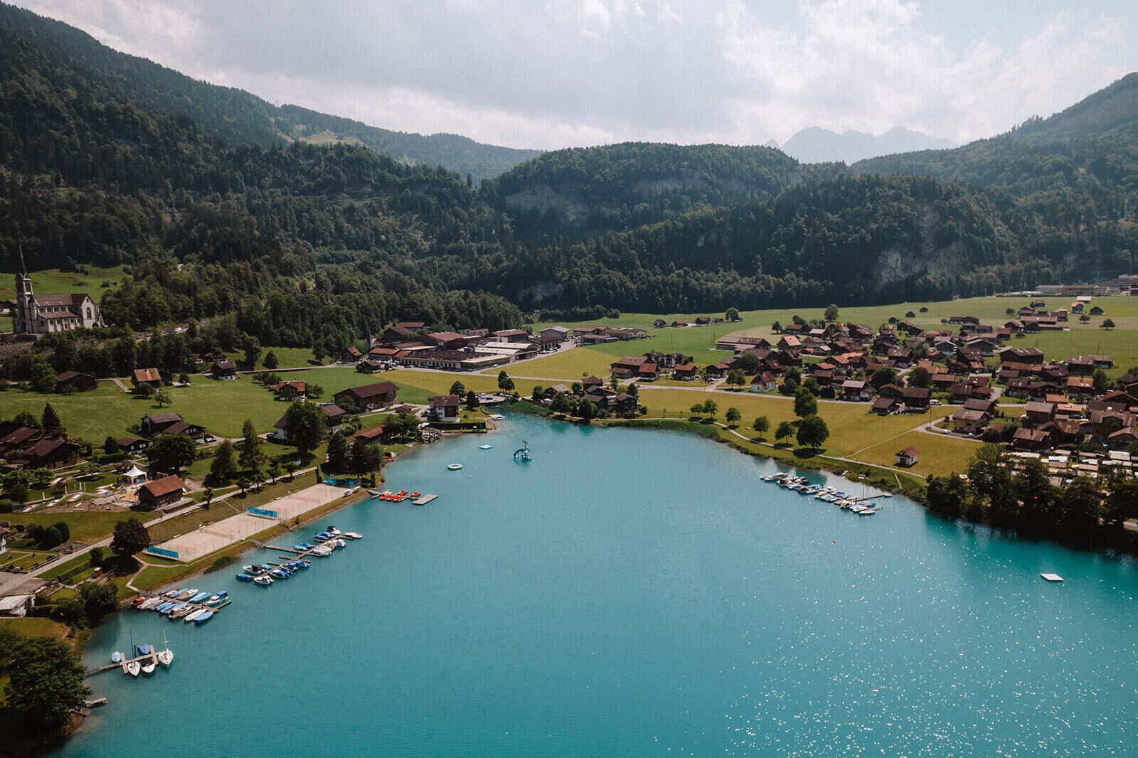 Vista aérea de un pueblo a orillas de un lago con casas, una iglesia y un puerto deportivo.