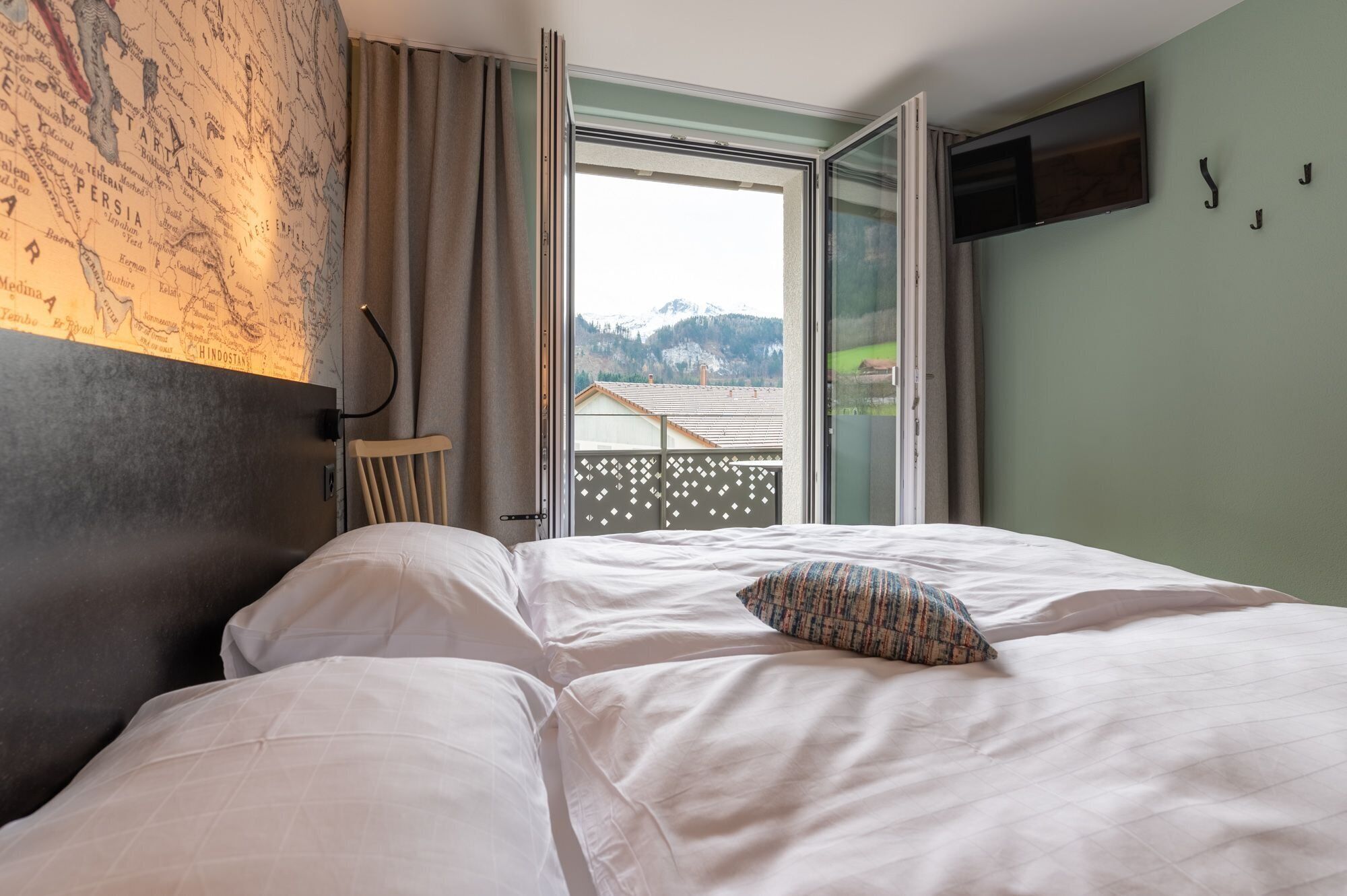 Ett hotellrum med en säng, en stol, en tv och utsikt över ett bergigt landskap.