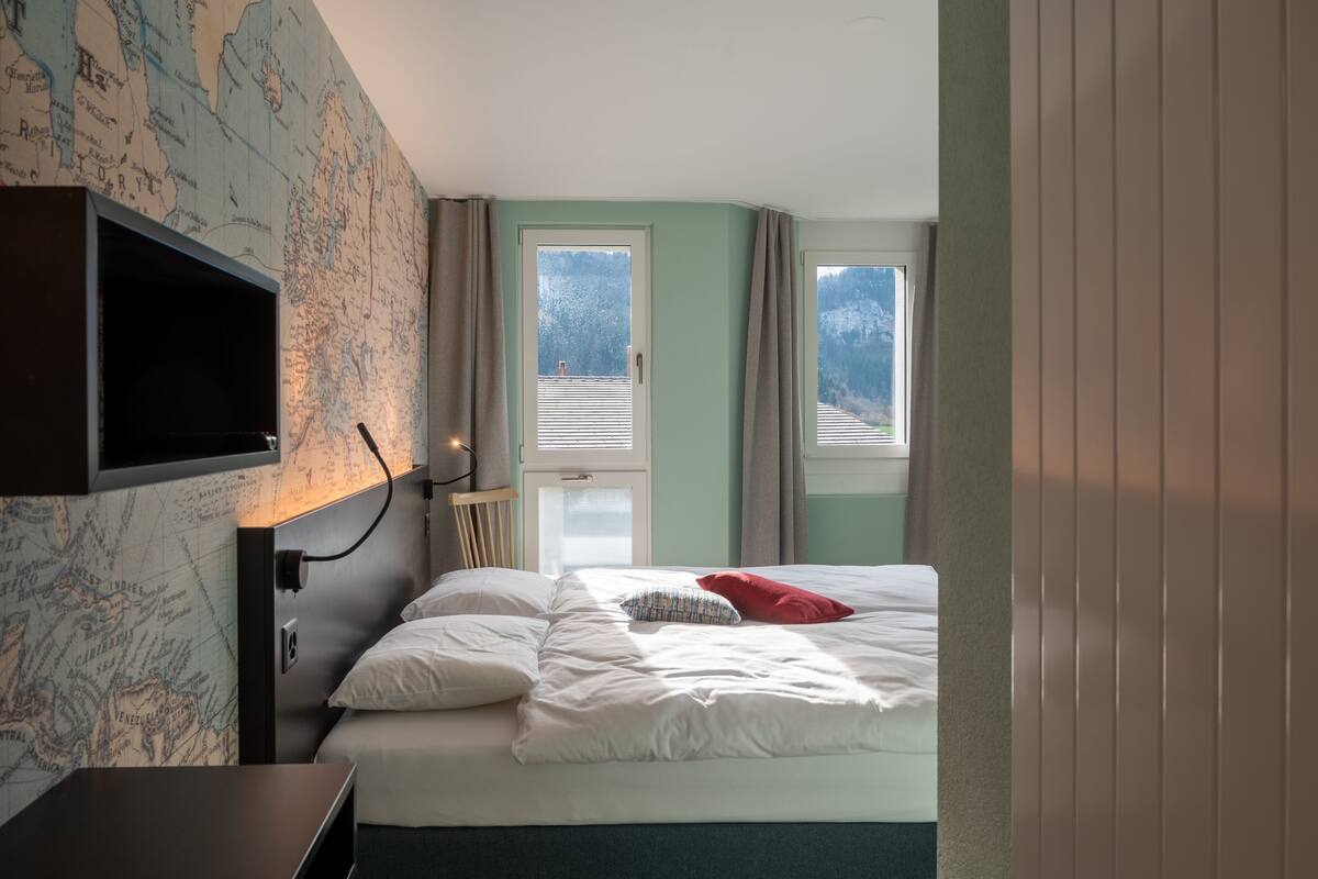 Un dormitorio con una cama, un mapa en la pared y dos ventanas.