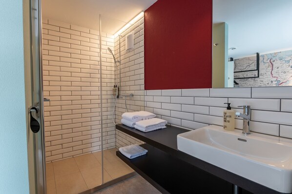 A modern bathroom with a white brick wall, a black countertop, a white sink, and a red accent wall. - Emma's B&B LUNGERN - Self Check-in Hotel (Lungern)