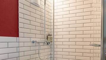 Een moderne badkamer met een douchecabine van glas, witte wandtegels in metro-stijl en een zwart aanrechtblad met handdoeken.