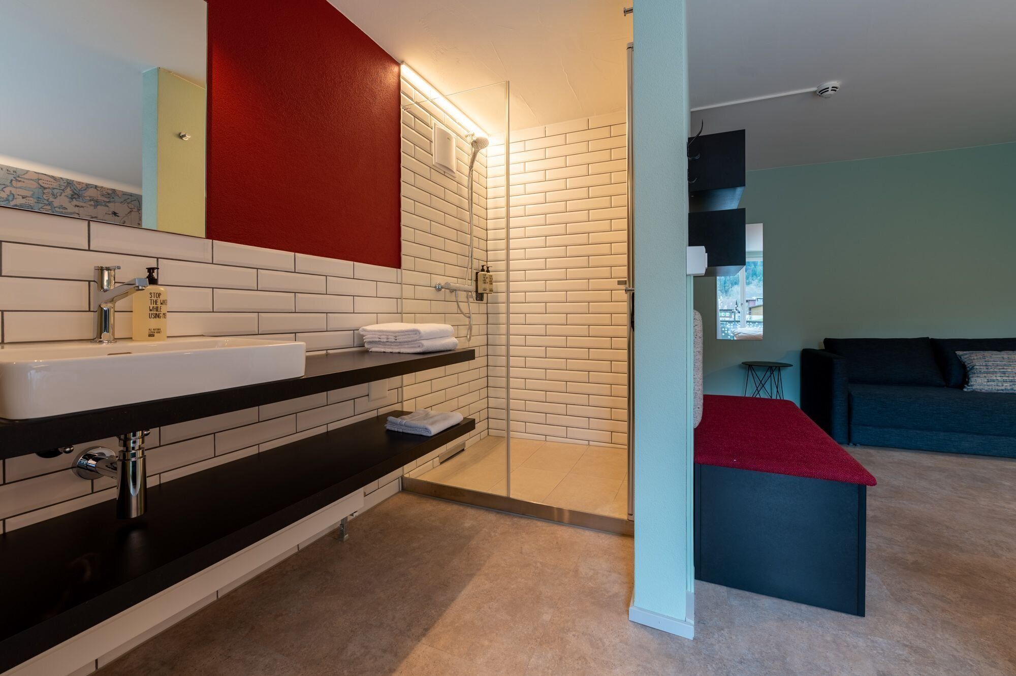 Une salle de bain moderne avec un mur recouvert de carreaux blancs, un plan de toilette noir et un mur d’accent rouge.