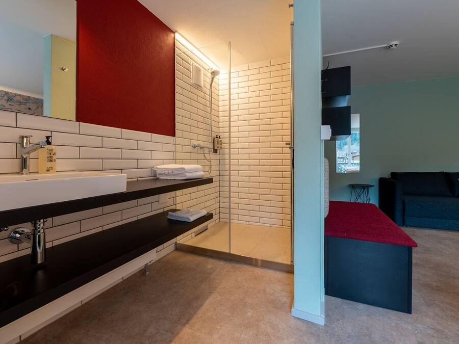 Une salle de bain moderne avec un mur recouvert de carreaux blancs, un plan de toilette noir et un mur d’accent rouge.