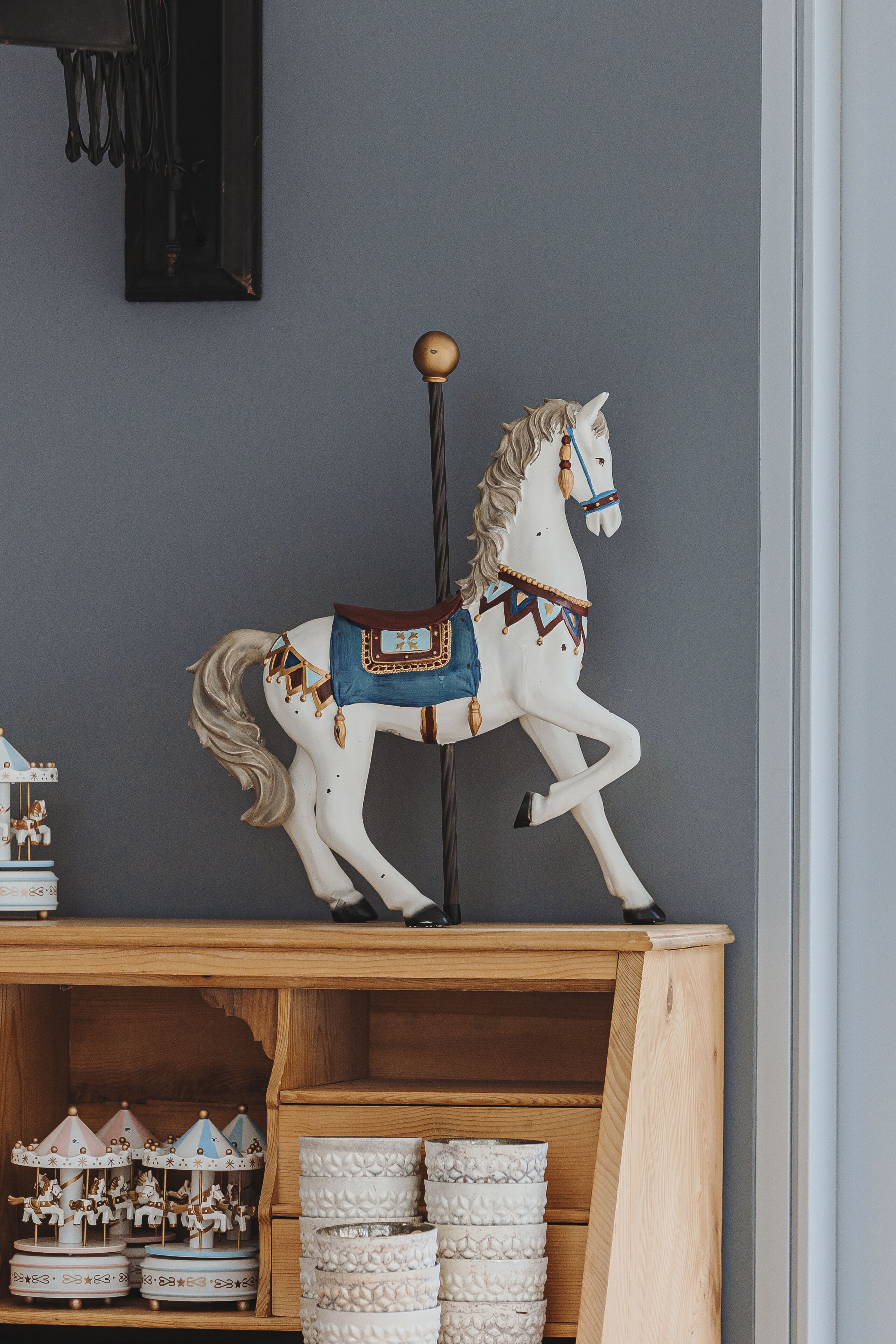 A carousel horse on a shelf, a wooden cabinet with storage baskets, and a carousel with horses.