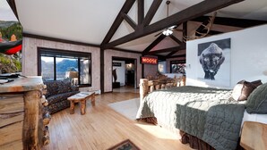 Een ruime kamer met een groot bed, een houten bank en uitzicht op de bergen.