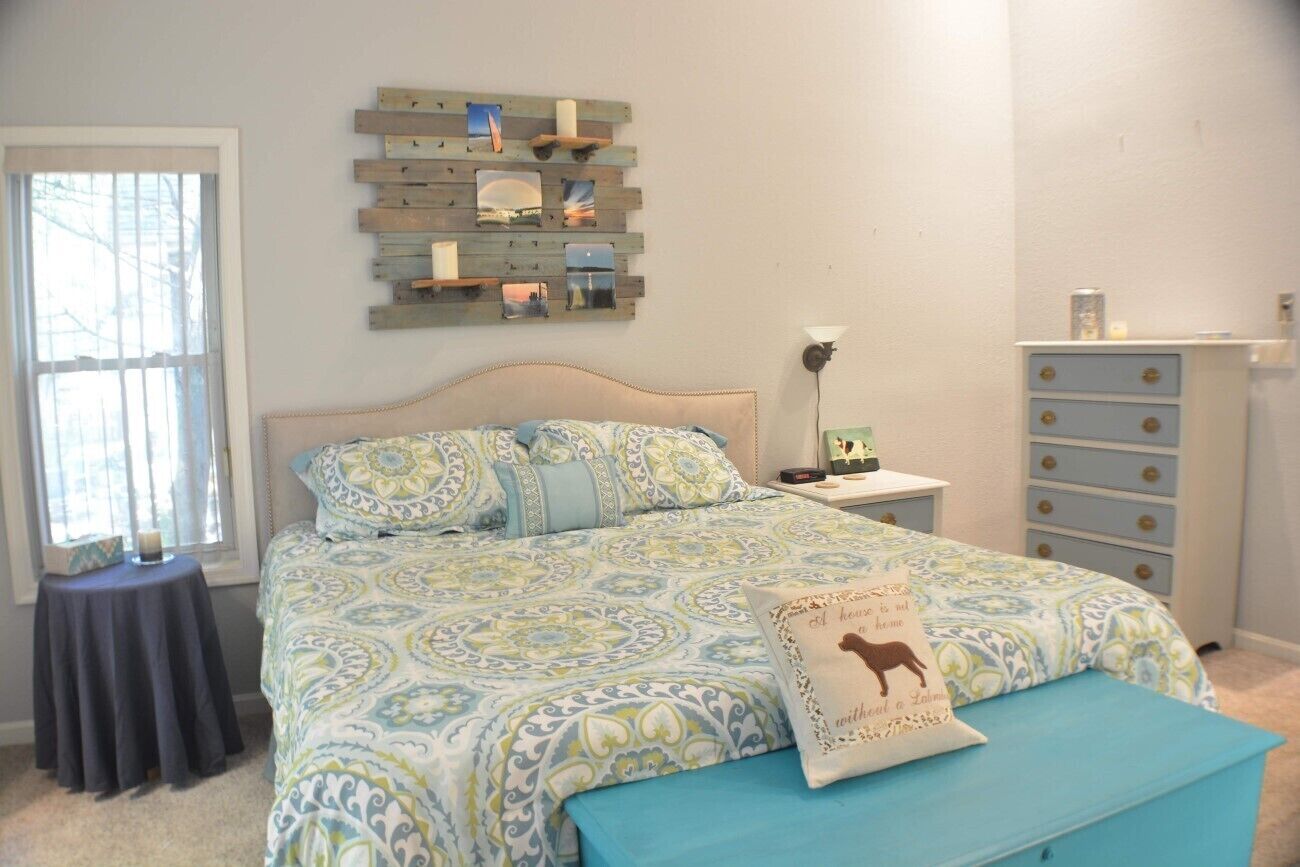 A bedroom with a bed, a bedside table, a dresser, and a wall-mounted photo display.