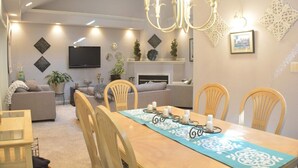 A dining area with a wooden table, chairs, and a chandelier. There are sofas and a TV in the background. - Home Away From Home,  pet friendly retreat! (Ocean Pines)