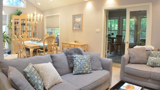 A living room with a grey sofa, a dining area with a wooden table and chairs, and a chandelier. - Home Away From Home,  pet friendly retreat! (Ocean Pines)