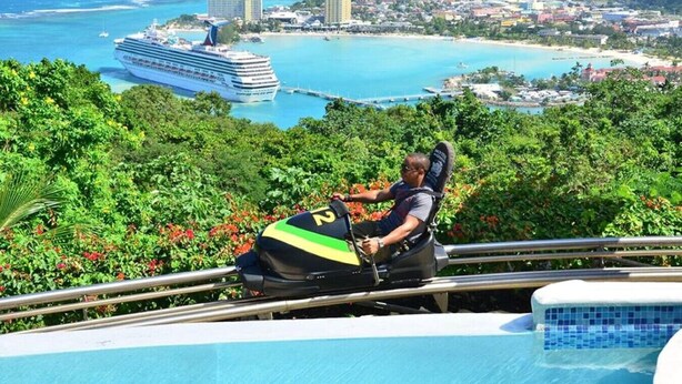 Un hombre en un telesilla con vistas a un crucero, una playa y un paisaje urbano.