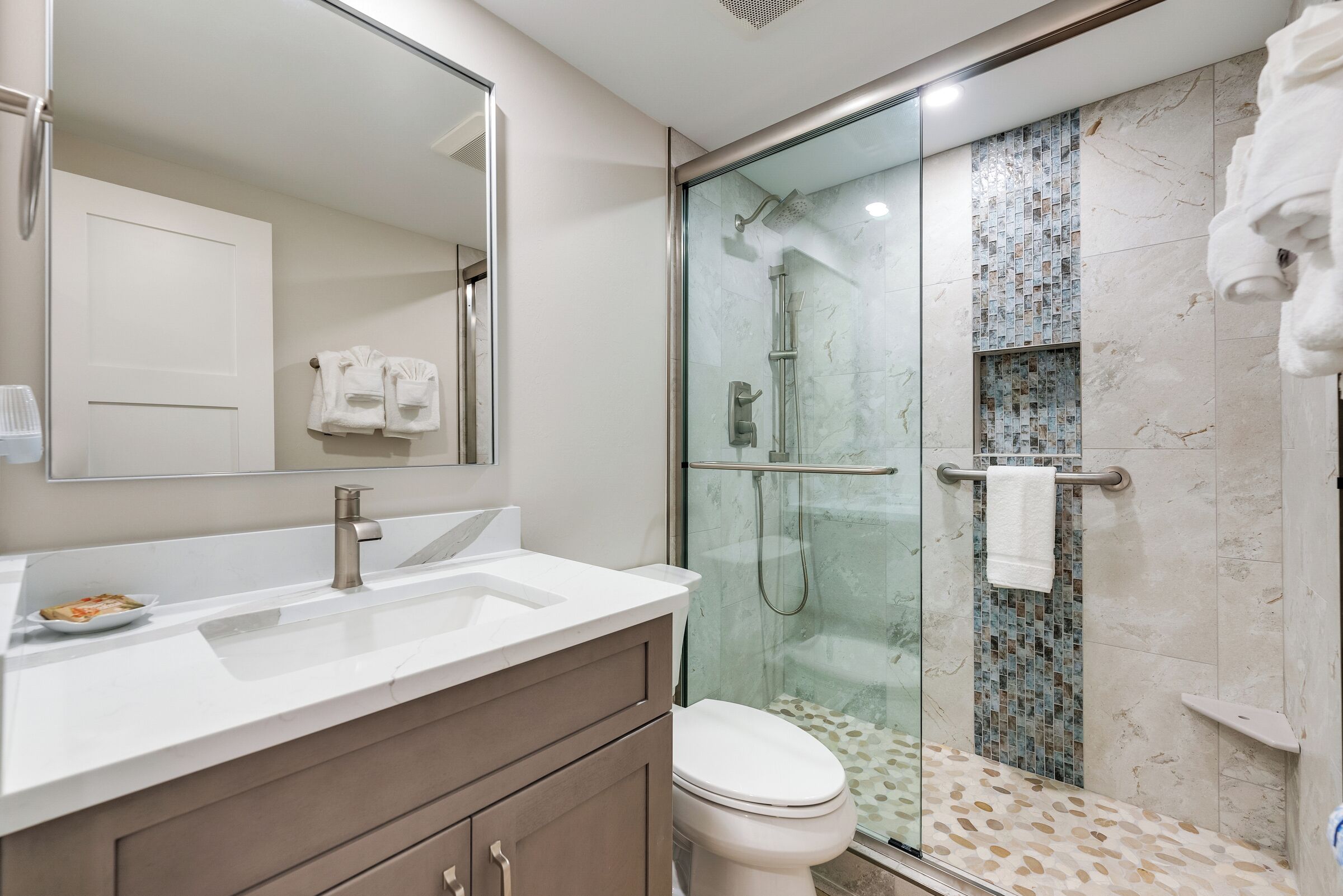 A modern bathroom with a glass-enclosed shower, a white sink, and a large mirror.