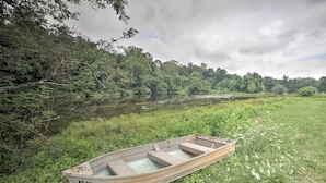 A rowboat with the inscription "NC 7397 WM" on its side, resting on grassy terrain beside a calm body of water, surrounded by dense greenery and trees. - Blue Ridge Nature Lovers retreat (Callaway)