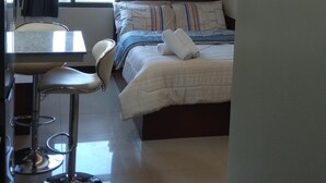 Una moderna camera d'albergo con un letto, una scrivania e una sedia. Si vede una finestra con tende, un condizionatore d'aria e una luce a soffitto.