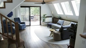 Un vaste salon agrémenté d’un escalier en bois, d’un canapé gris, d’un fauteuil bleu et d’un coin repas avec une table et des chaises.
