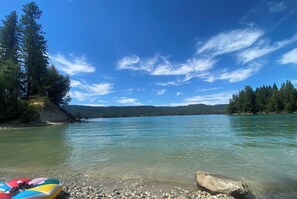 A clear lake with a rocky shore, surrounded by dense forest and hills.