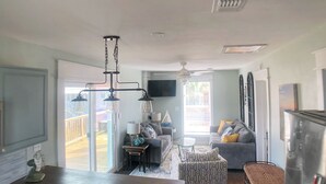Ein geräumiges Wohnzimmer mit großem Fenster, Deckenventilator, Flachbildfernseher und Essbereich mit Holztisch.