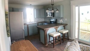 Eine moderne Küche mit hellblauen Schränken, einer zentralen Kochinsel mit Barhocker, einem Kühlschrank und einem Essbereich mit Korbsessel und Sofa.