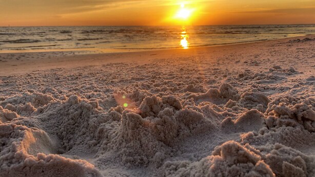 Ein Strand mit Dünen und einem Sonnenuntergang im Hintergrund.