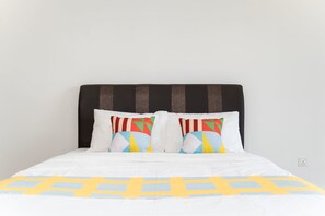 A bed with a white bedspread and colorful geometric pillows.