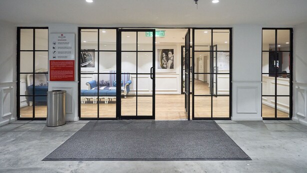 A hotel entrance with a glass door, a welcome mat, a trash bin, and a poster on the wall. - OYO Home 44050 Essential Studio Empire Marriot (Petaling Jaya)