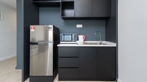A compact kitchen with a stainless steel refrigerator, a microwave, a sink, and black cabinetry. - OYO Home 44050 Essential Studio Empire Marriot (Petaling Jaya)